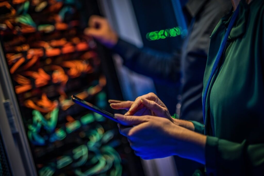 Male and female IT engineers checking servers in server room with help of tablet.