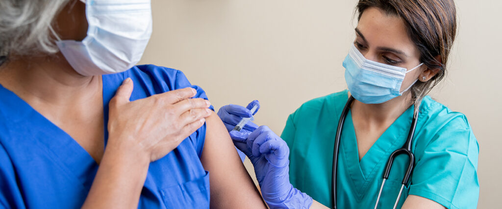 Nurse gives senior adult healthcare worker the Covid-19 vaccine