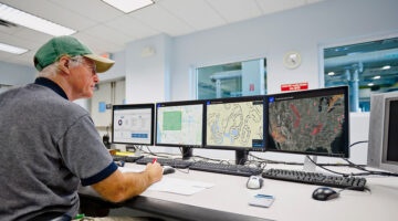 Tech in a ballcap monitors tornado data on multiple monitors