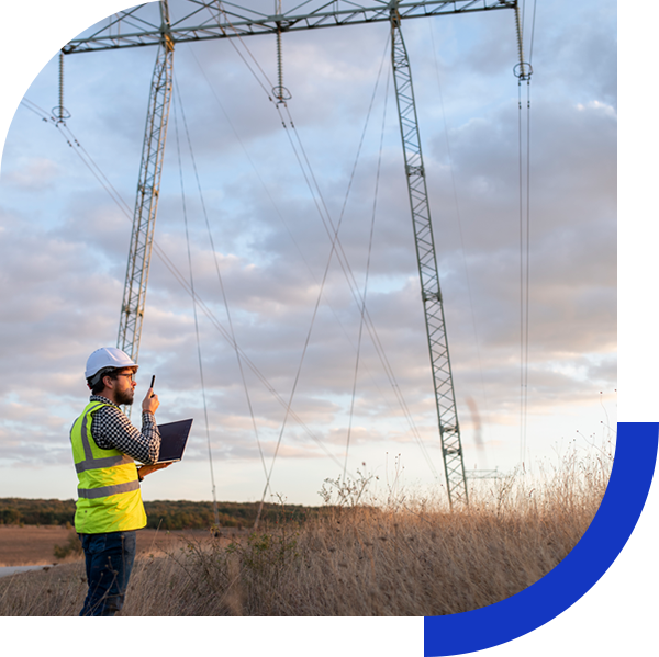 Electrician on phone standing in a field under high power line tower.