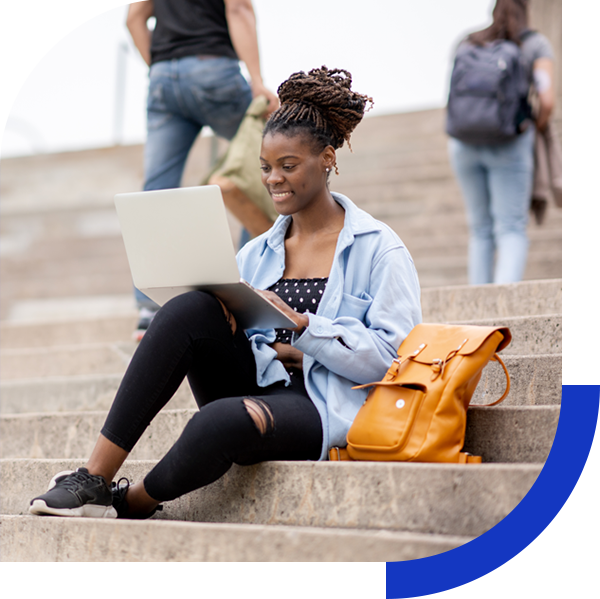 College student on university steps viewing a laptop with a smile