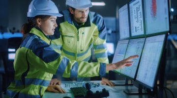 Industry 4.0 Modern Factory: Project Engineer Talks To Female Operator Who Controls Facility Production Line, Uses Computer With Screens Showing Ai, Machine Learning Enhanced Assembly Process